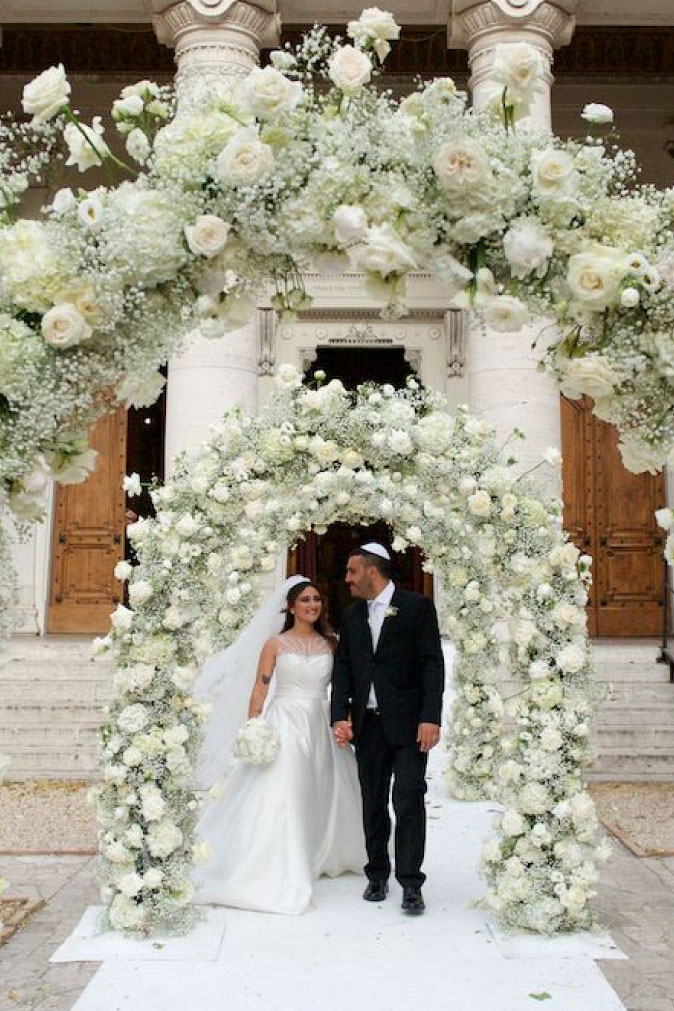 Sposi felici sotto un arco floreale - Servizio di grafica per matrimonio e wedding stationery su misura